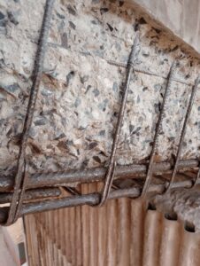 Exemplo real de degradação do concreto armado com armadura exposta e sinais visíveis de corrosão em estrutura industrial